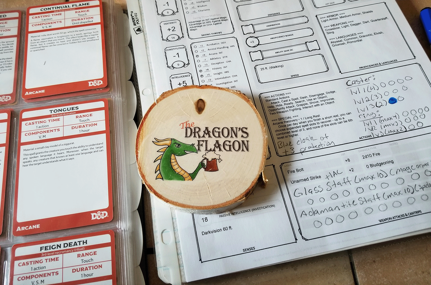 Image of Dragon's Flagon Logo on a round wooden coaster sitting on a character sheet